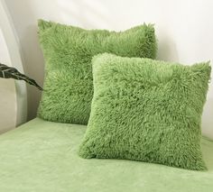 two green pillows sitting on top of a bed next to a plant in a vase