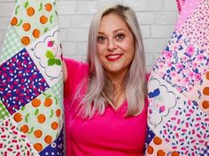 a woman in pink shirt holding up several colorful quilts