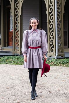 a woman in a dress and hat is walking down the street with her hand on her hip