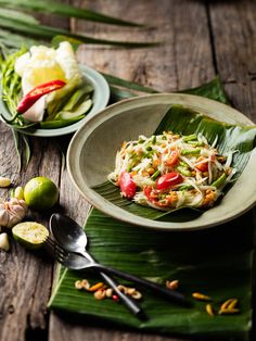 two plates with food on them sitting on top of a wooden table next to green leaves