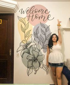 a woman is standing in front of a welcome home sign with flowers and leaves painted on it