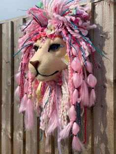 a stuffed animal with pink hair on top of a wooden fence next to a wall