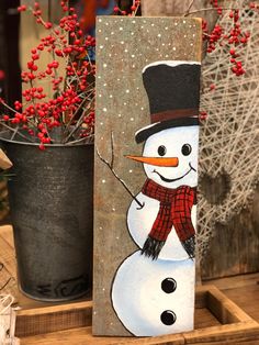 a wooden block with a snowman painted on it and red berries in the background