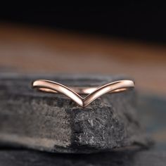 a rose gold wedding band on top of a black stone slab, with an elegant curved design in the middle