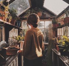 a woman standing in front of a greenhouse filled with potted plants and looking out the window