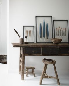 a wooden table topped with pictures next to two stools and a bowl filled with feathers