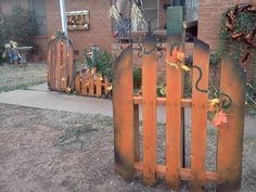 an orange wooden fence sitting in front of a brick house with autumn decorations on it