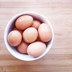 a white bowl filled with brown eggs on top of a wooden table