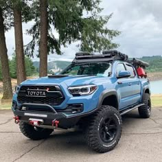 a blue toyota truck parked in front of some trees with a person standing next to it