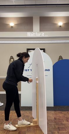 a woman standing next to a white surfboard on top of a wooden stand in a room