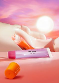 an orange and pink lip sitting next to a tube of grape oil on a pink surface