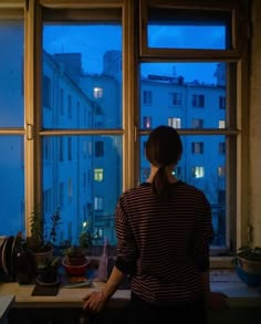 a woman standing in front of a window looking out at the city outside her house