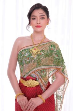 a woman in a red and green dress with gold jewelry on her head, standing next to a white curtain