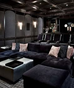 a home theater with black couches and grey ottomans in the middle of it