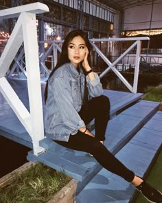 a young woman sitting on top of a wooden bench next to a white structure at night