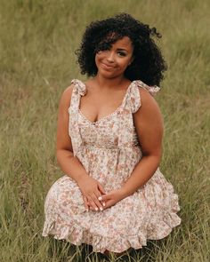 a woman sitting in the grass with her hands on her knees and looking at the camera