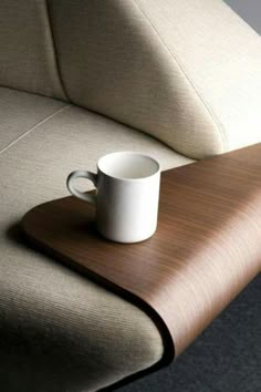 a white coffee cup sitting on top of a wooden table next to a beige couch