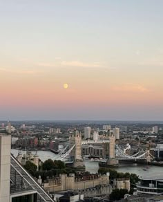 the moon is setting over london, england as seen from the top of tower bridge