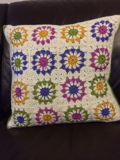 a crocheted pillow on a black leather couch with a white and multicolored flower design