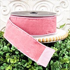 a pink ribbon is sitting on top of some green plants and a white plate with a wooden bead