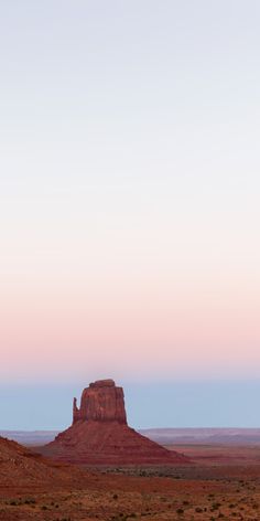 a lone horse is standing in the desert at sunset with a distant rock formation behind it