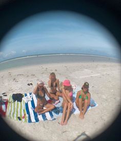 three women sitting on a towel at the beach in front of an object that looks like a fish eye lens