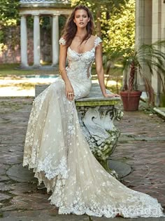 a woman sitting on top of a bench wearing a wedding dress with white lace and appliques