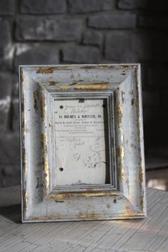 an old photo frame sitting on top of a wooden table next to a brick wall