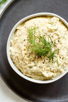 a black plate with a bowl of hummus and dill garnish on it