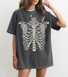 Skeleton Rib Vintage Graphic T-Shirt, Rib Cage Shirt, Retro Skeleton Tee, 90s Skull Shirt, Spooky Shirt, Halloween gift Comfort Colors® F I T ∙ & ∙ S I Z I N G : -->These Unisex T-shirts have a modern-fit. Consult the size chart in the pics for an accurate fit. -->Women's sizes are narrower than the waist. -->Sleeves are rolled up in some product pictures. They do not come rolled up on delivery. T I M E ∙ T O ∙ D E L I V E R Y : -->Processing and production time is 1-2 business days. -->Delivery Edgy Halloween Tops With Relaxed Fit, Edgy Halloween Relaxed Fit Tops, Edgy Relaxed Fit Halloween Tops, Grunge Short Sleeve Tops For Halloween, Punk Style Relaxed Fit Tops For Halloween, Relaxed Fit Punk Tops For Halloween, Skeleton Shirt Outfit, Halloween Grunge Short Sleeve Tops, Edgy Oversized Tops For Halloween