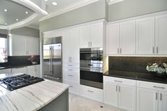 a large kitchen with white cabinets and marble counter tops, along with an island in the middle