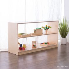 a wooden shelf with toys on it in front of a white curtained window and potted plant