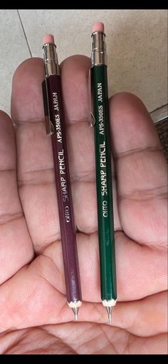 two pencils in the palm of someone's hand, one is purple and one is green