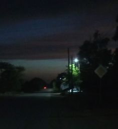 a street at night with cars parked on the side of the road and trees in the background