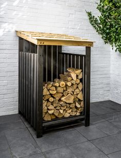 a stack of logs sitting in front of a white brick wall next to a tree