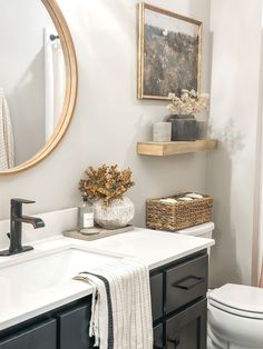 a white toilet sitting next to a bathroom sink under a round mirror on top of a wooden shelf