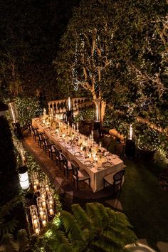 an outdoor dinner table is lit up at night with candles and greenery around it