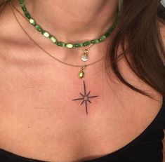 a woman's chest with a star tattoo on the top and green beads around her neck