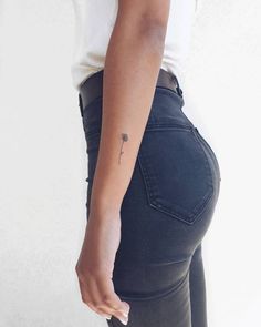 a woman with a small flower tattoo on her left arm and right hand behind her back