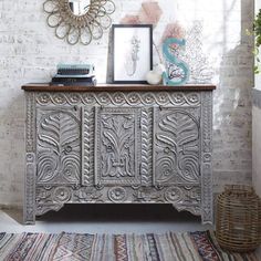 an ornately decorated sideboard stands in front of a brick wall with a mirror above it