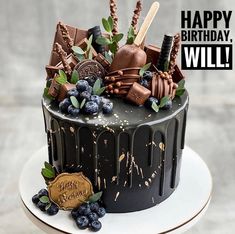 a birthday cake with chocolate and blueberries on the top is decorated with an assortment of desserts