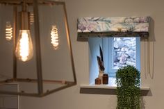 a lamp hanging from the side of a window next to a potted plant on a shelf