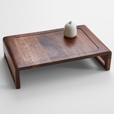 a wooden table with a white vase on top and one piece of wood sitting on it