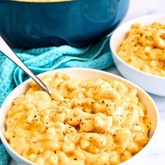 two bowls filled with macaroni and cheese on top of a blue towel next to a pot