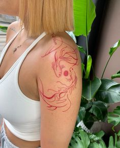 a woman with a dragon tattoo on her upper arm and shoulder, next to a plant