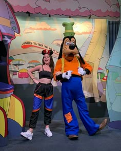 two people standing next to each other in front of mickey mouse