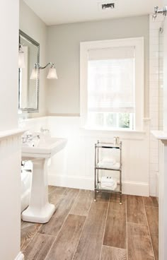 a bathroom with white fixtures and wood flooring, including a pedestal sink in the center