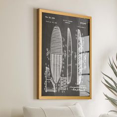 a drawing of a surfboard hangs on the wall next to a chair and potted plant