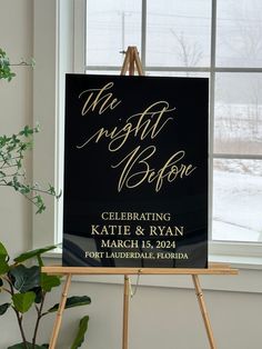 a black and gold wedding sign sitting on top of a easel next to a window