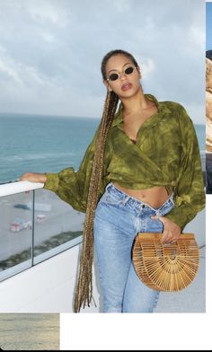 a woman standing on top of a balcony next to the ocean holding a straw bag